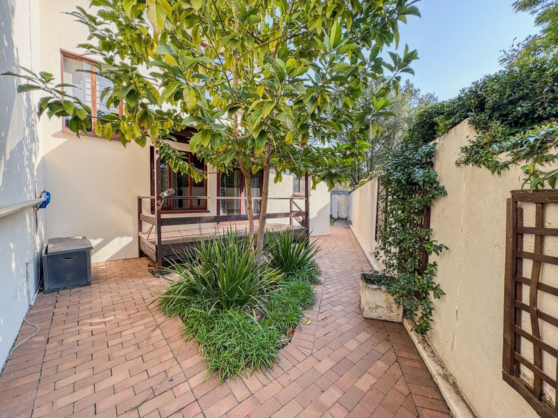A private rear courtyard featuring brick paving, a small timber deck, and established garden elements enclosed by a boundary wall.