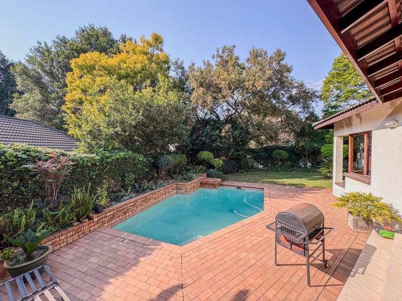 Outdoor pool area featuring a brick-paved patio, a swimming pool with brick surround, and a landscaped garden with mature trees.