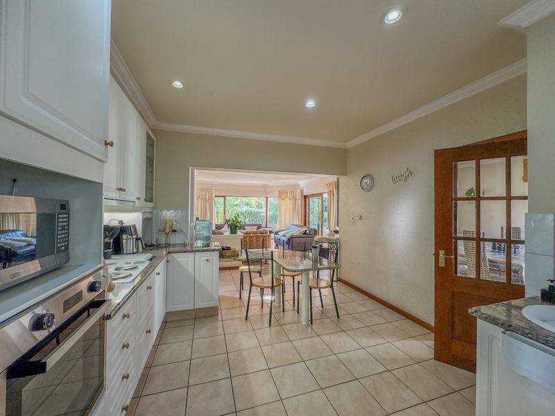 Open plan kitchen and dining area featuring white cabinetry, granite countertops, built-in appliances, and tiled flooring, flowing into the adjacent living space.