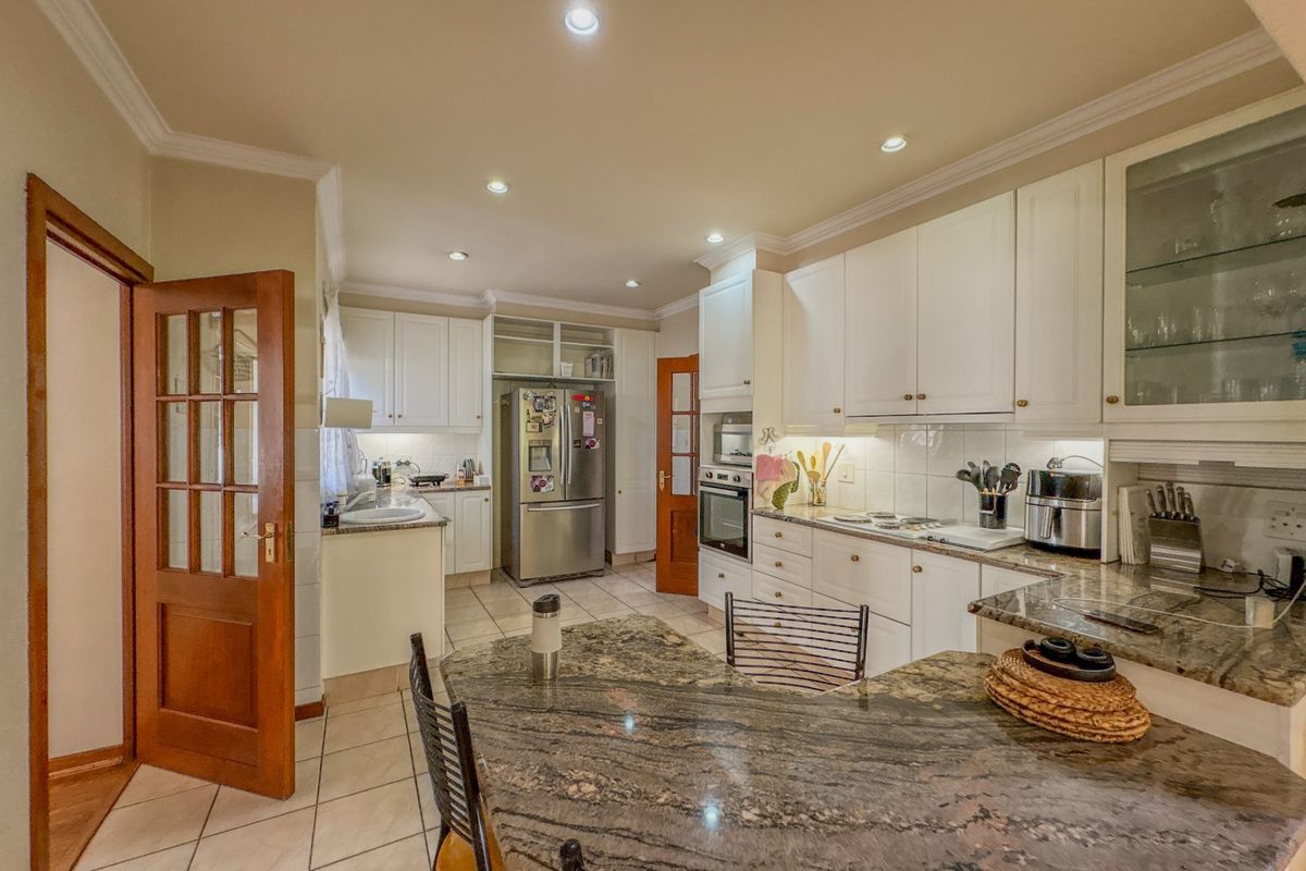 A well-appointed kitchen featuring granite countertops, built-in cabinetry, integrated oven and hob, and recessed lighting, offering a functional and classic culinary space.