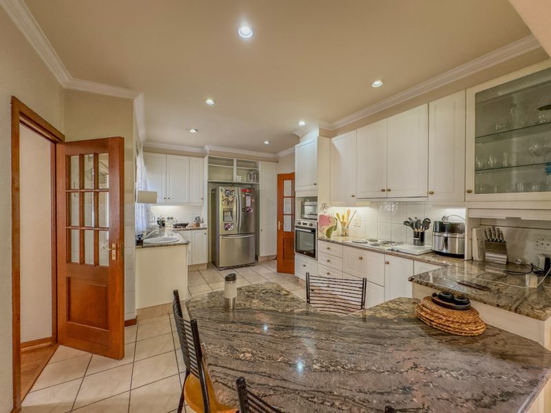 A well-appointed kitchen featuring granite countertops, built-in cabinetry, integrated oven and hob, and recessed lighting, offering a functional and classic culinary space.