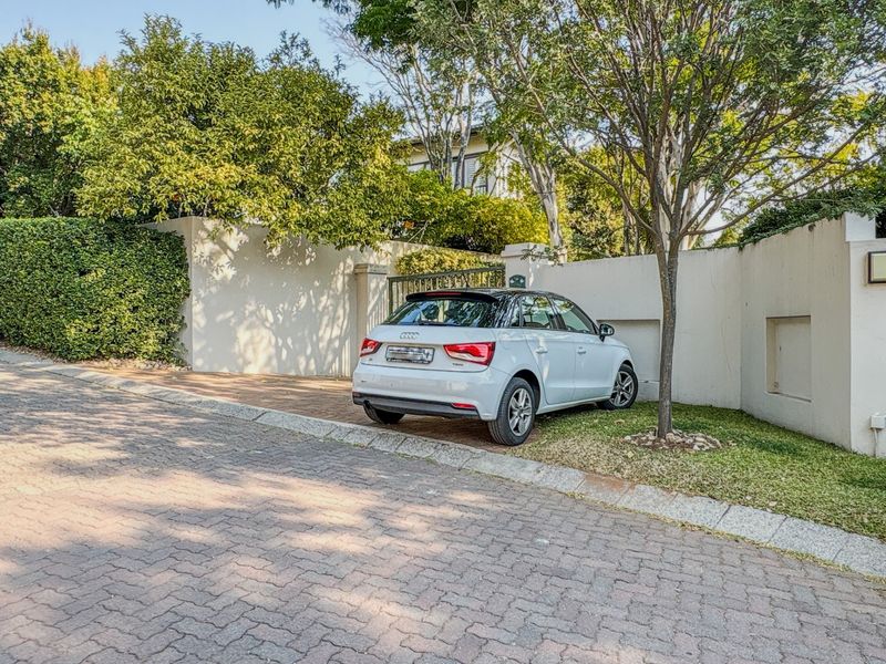 Front exterior view of the property featuring a paved driveway, boundary wall, and gated entrance.