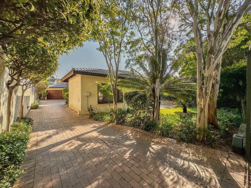 A view of the rear exterior featuring a paved driveway, mature trees, and a well-maintained garden area adjacent to the property structure.