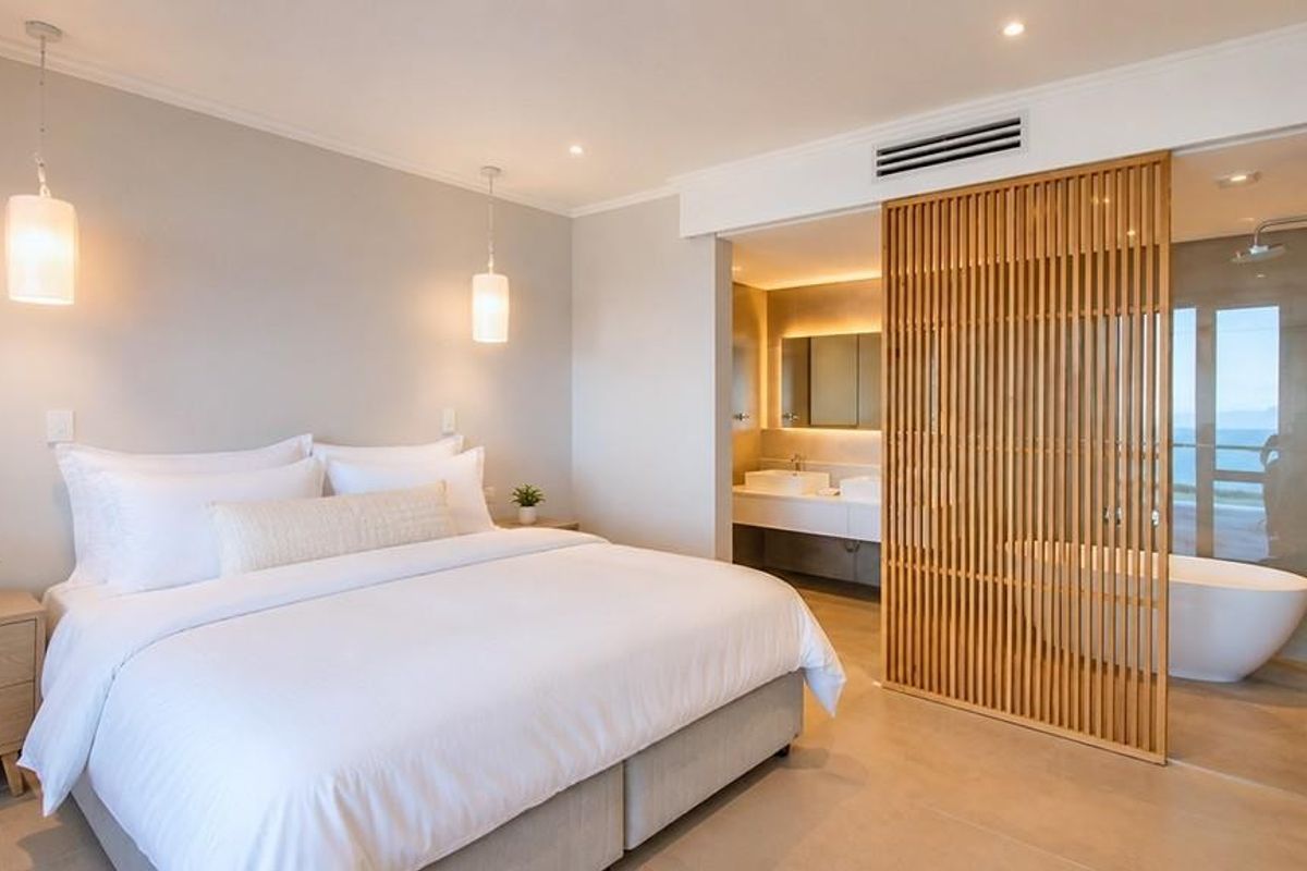 Modern bedroom featuring a timber slat divider, open-plan ensuite with a freestanding bathtub, walk-in shower, and double vanity with contemporary finishes.