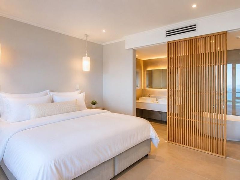 Modern bedroom featuring a timber slat divider, open-plan ensuite with a freestanding bathtub, walk-in shower, and double vanity with contemporary finishes.