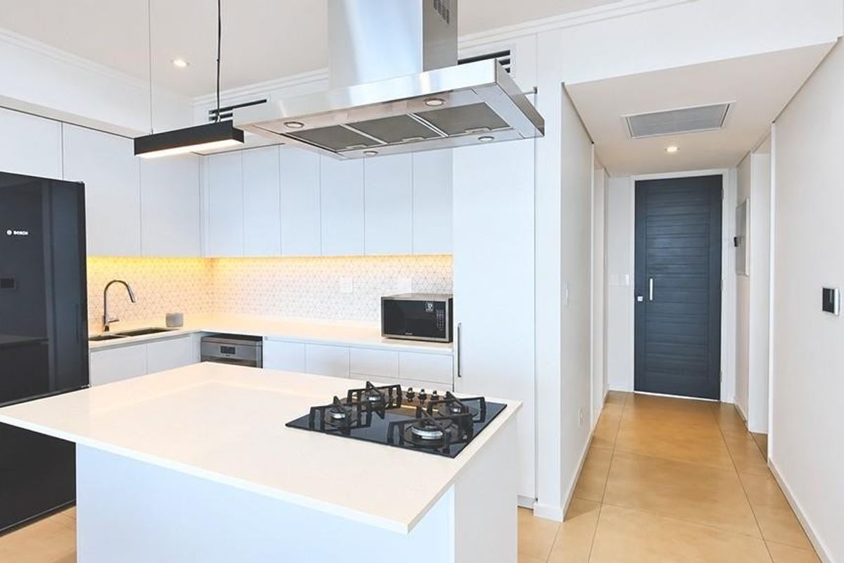 Modern kitchen featuring a central island with gas hob, sleek white cabinetry, quartz countertops, and high-quality stainless steel appliances in a bright, contemporary space.