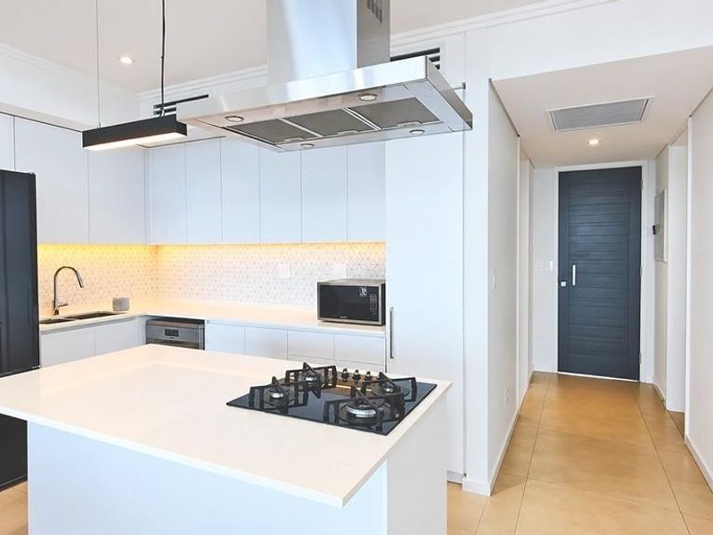Modern kitchen featuring a central island with gas hob, sleek white cabinetry, quartz countertops, and high-quality stainless steel appliances in a bright, contemporary space.