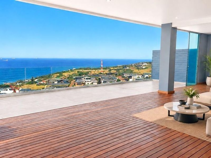 Expansive covered balcony featuring premium timber decking, a frameless glass balustrade, and panoramic ocean views, seamlessly connecting indoor and outdoor living spaces.