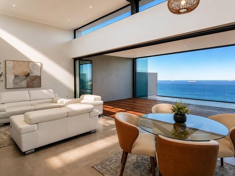 Spacious open-plan living area featuring high ceilings, clerestory windows, and seamless transition to a large balcony with expansive ocean views.