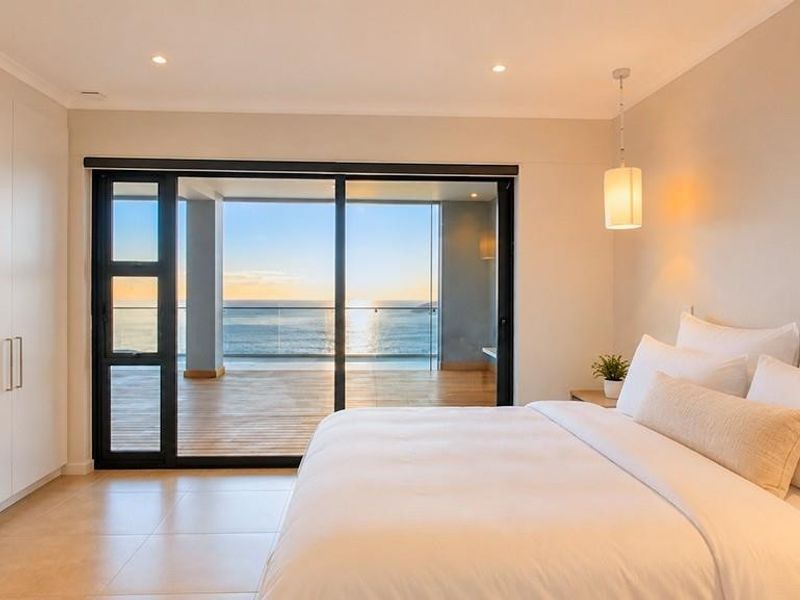 Modern bedroom featuring built-in cupboards, tiled flooring, and large sliding glass doors opening onto a balcony with ocean views.
