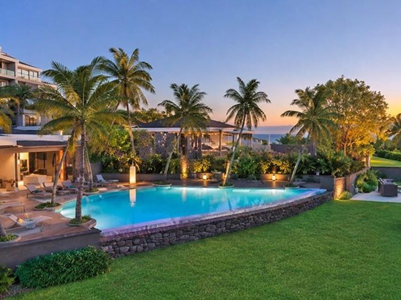 A luxury outdoor pool area featuring a stone-edged swimming pool, timber decking, and a stone fire pit set within a beautifully landscaped garden.