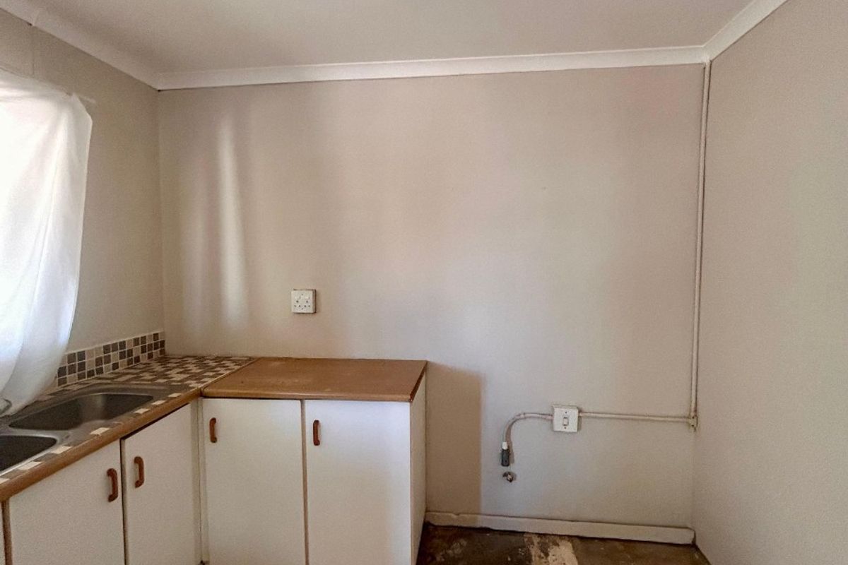 A compact kitchen area featuring built-in cabinetry, a stainless steel sink, and tiled flooring, currently requiring floor repairs and cosmetic updates.