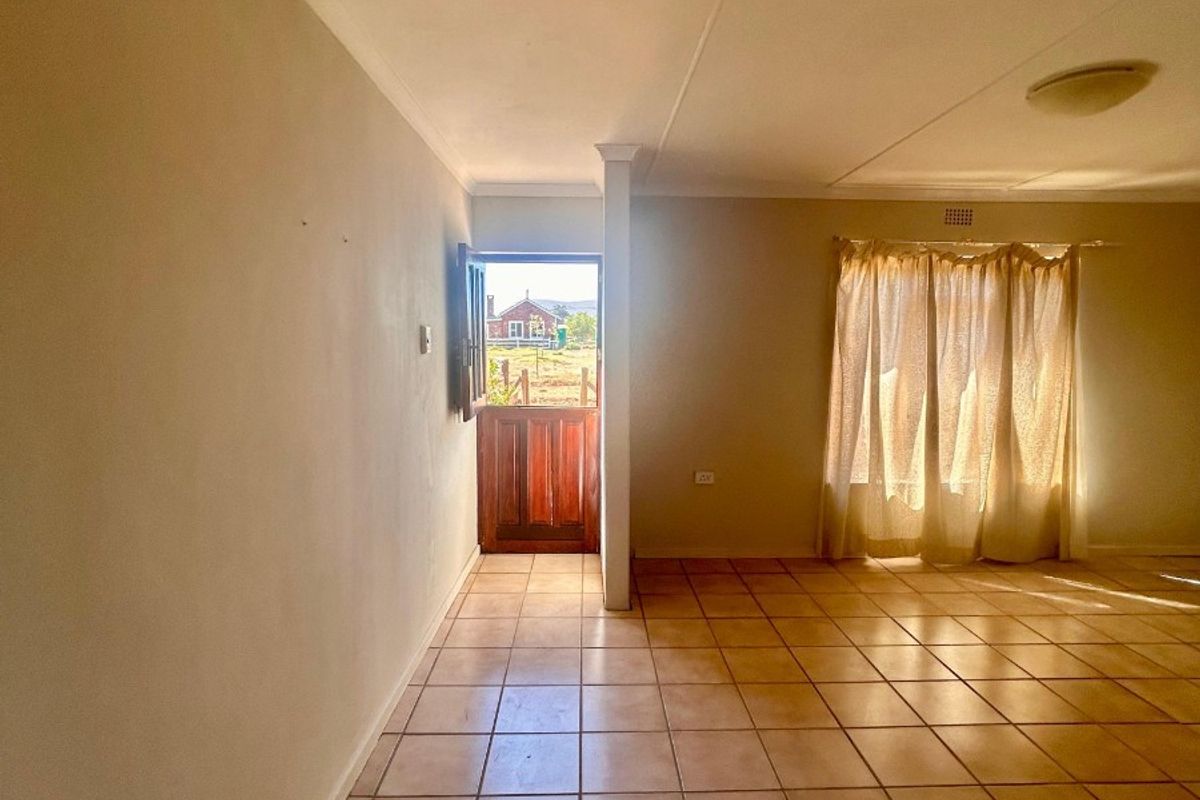 An empty living room featuring neutral walls, ceramic floor tiles, and a stable door leading to the exterior.