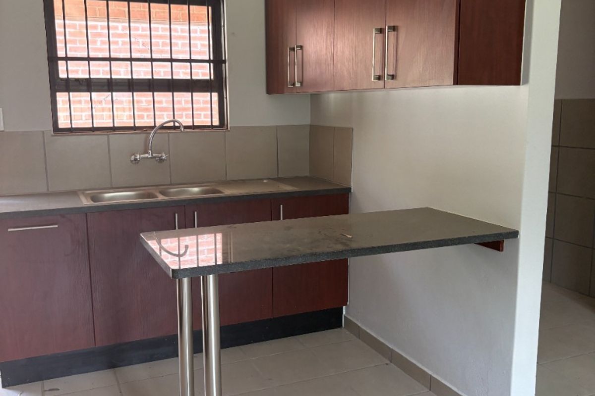 A functional kitchen featuring dark wood cabinetry, granite countertops, a breakfast bar, and tiled flooring, presented in a clean, empty state.