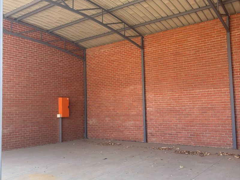 A spacious, open-plan utility area featuring exposed brick walls, a high-pitched corrugated metal roof with steel trusses, and a durable concrete floor.