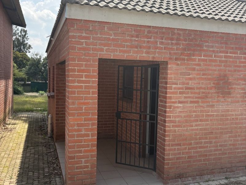 A detached brick utility structure featuring a tiled roof and a secure metal gate, situated on a paved area.