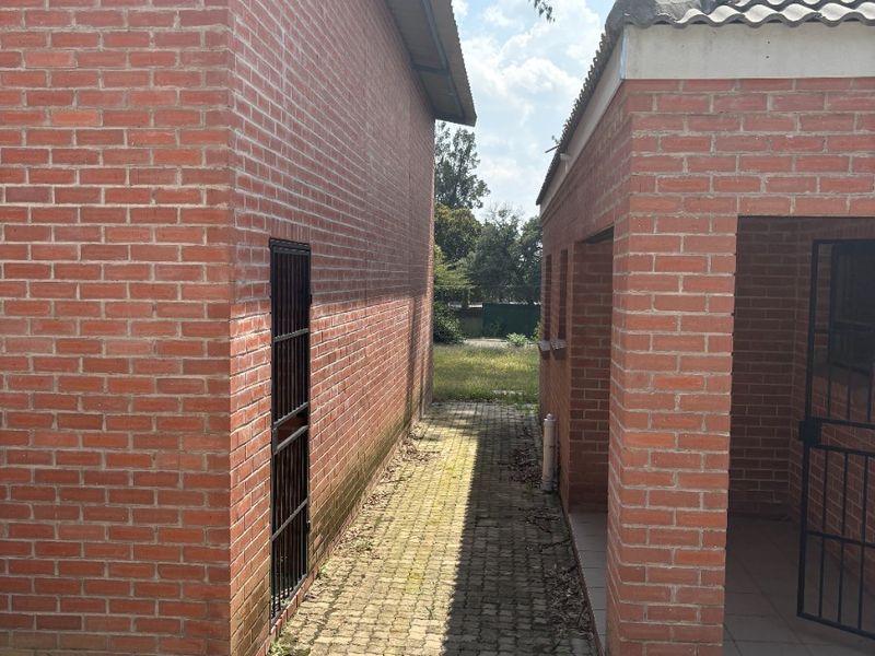 A narrow paved walkway between two face brick farm buildings, featuring security gates and tiled roofing.