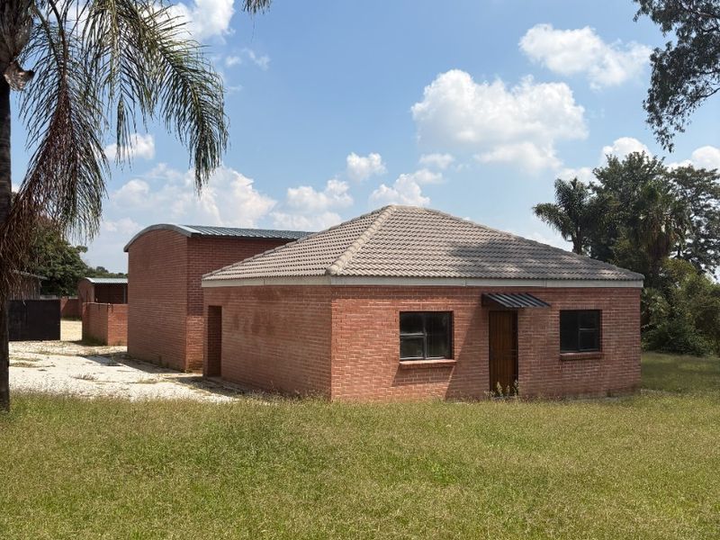 A view of the rear exterior of a face brick farm building featuring a hipped tiled roof and a secondary curved roof structure.