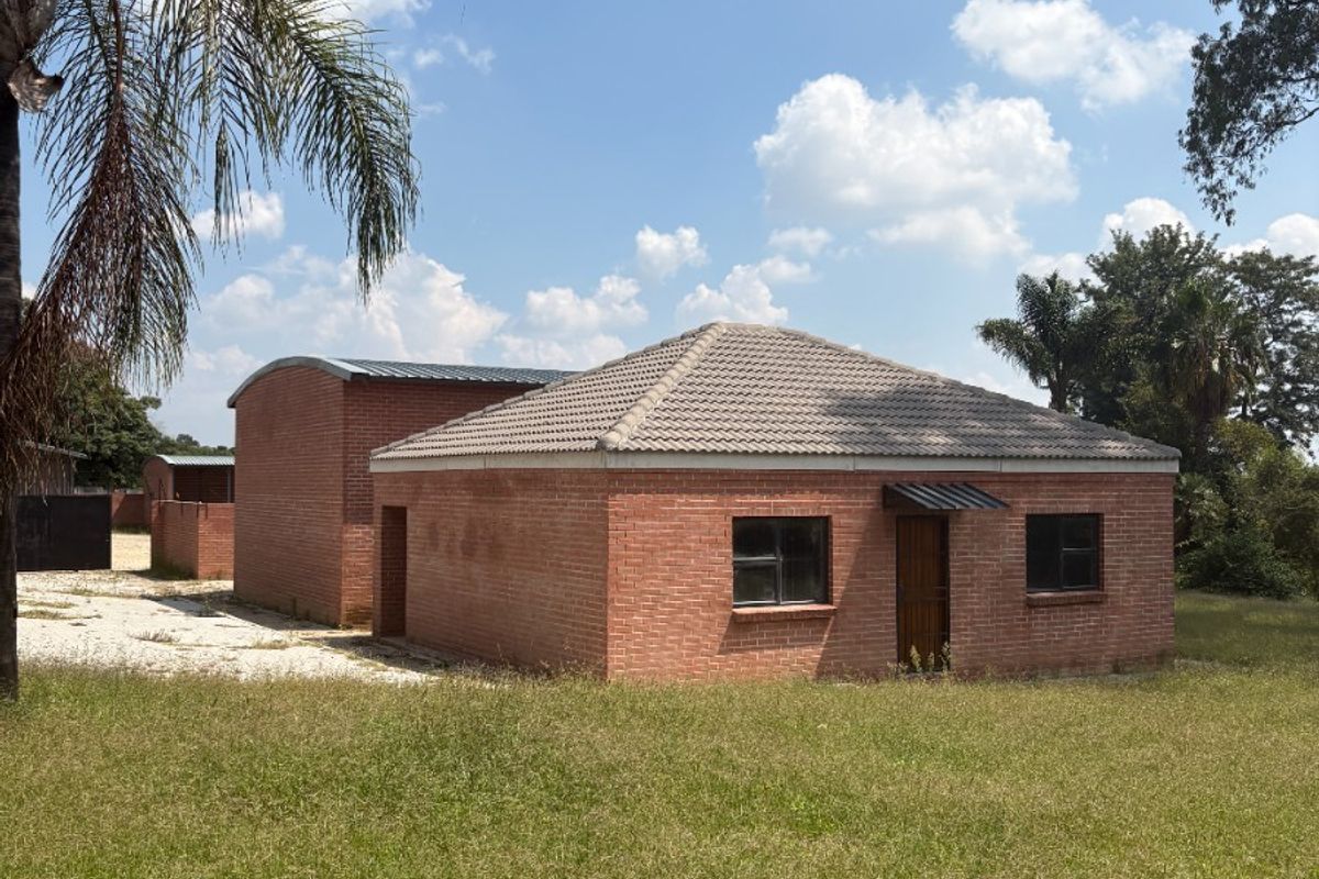 A view of the rear exterior of a face brick farm building featuring a hipped tiled roof and a secondary curved roof structure.