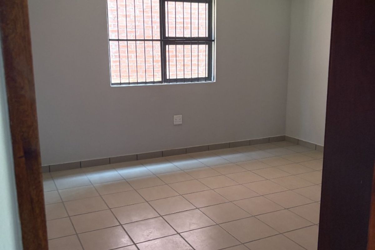 A clean, empty bedroom featuring neutral tiled flooring, white walls, and a window fitted with security bars.