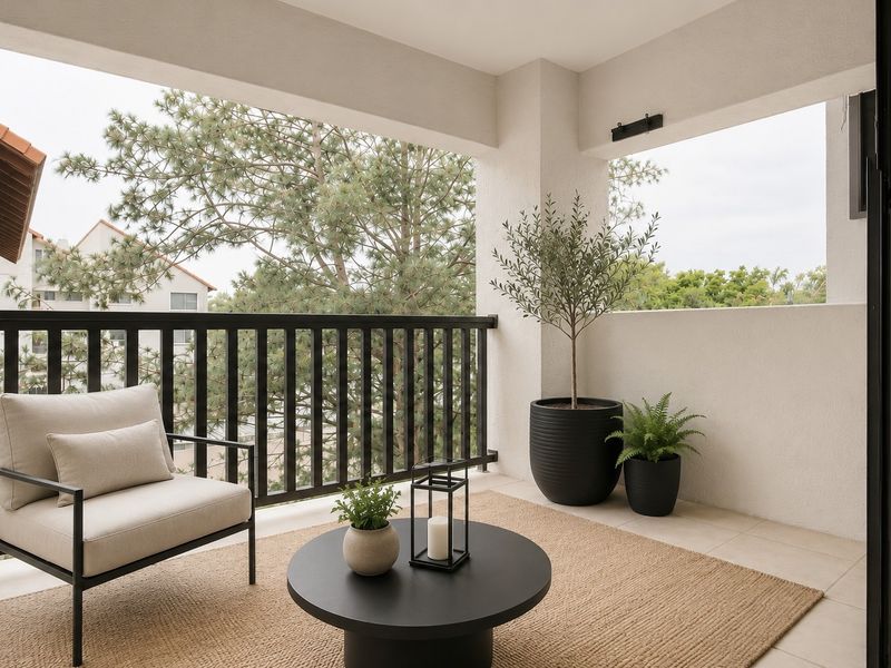 A well-maintained covered balcony featuring tiled flooring, a black metal railing, and an exterior wall light, offering a pleasant outdoor space.