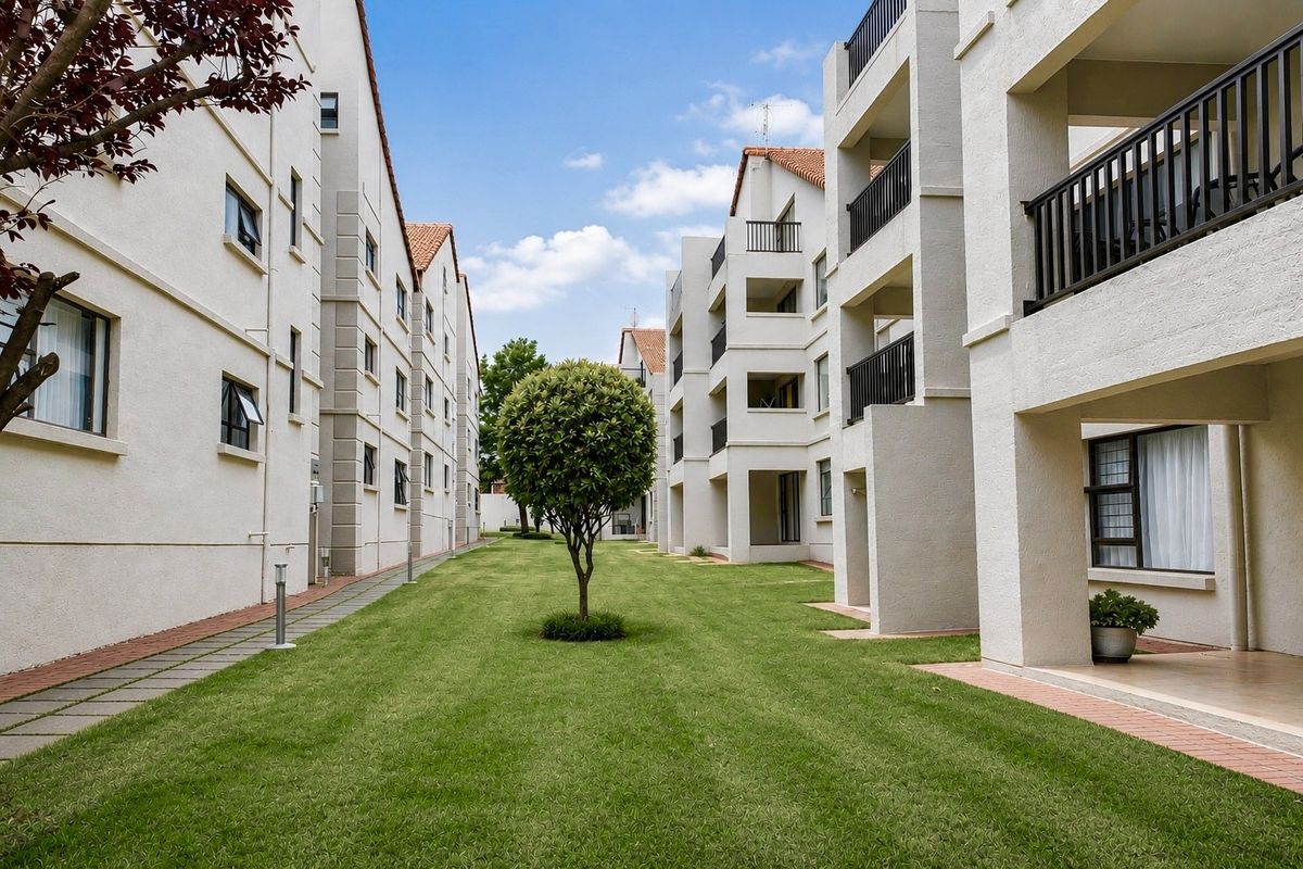 A well-maintained communal garden area between apartment blocks, featuring paved walkways, manicured lawns, and private balconies for the units.