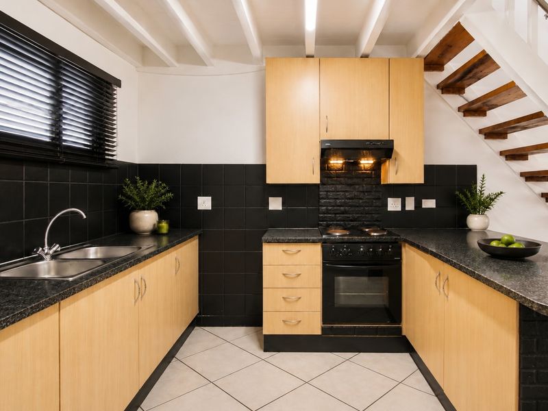 A functional kitchen featuring light wood cabinetry, black tiled backsplash, granite-look countertops, built-in oven and hob, and an adjacent staircase.