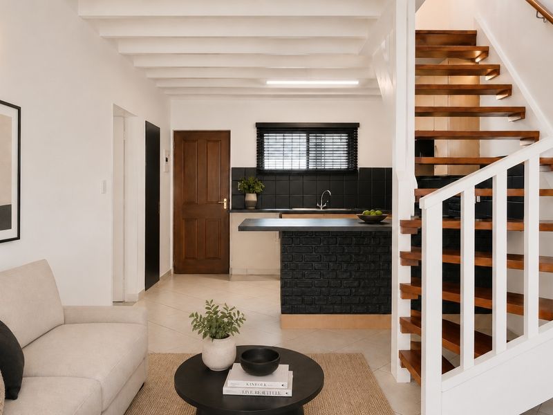 Open plan living area featuring a modern kitchen with a breakfast island, exposed ceiling beams, and a striking wooden staircase leading to the upper level.
