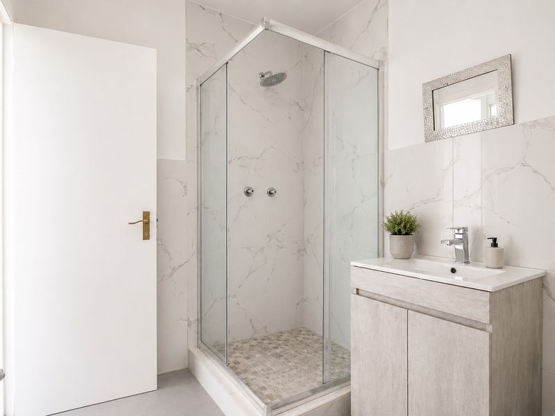Modern bathroom featuring a glass-enclosed shower, marble-look wall tiling, and a contemporary vanity unit with a basin.