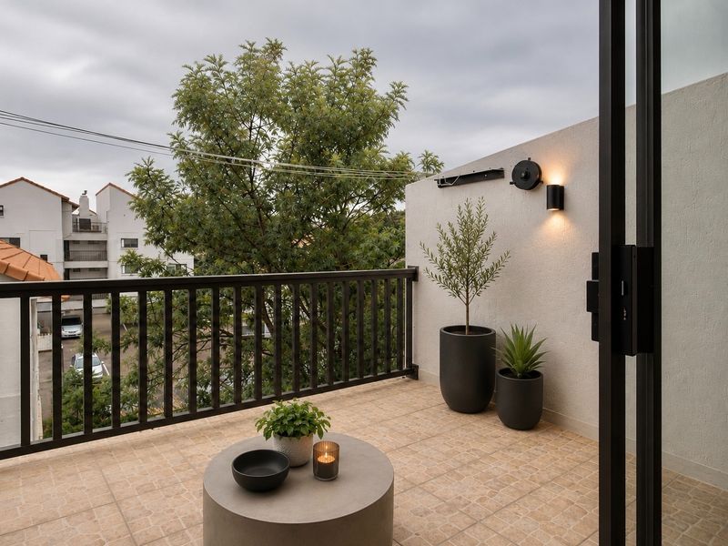 A well-maintained apartment balcony featuring tiled flooring, a secure metal railing, and wall-mounted lighting, offering a pleasant outdoor space.