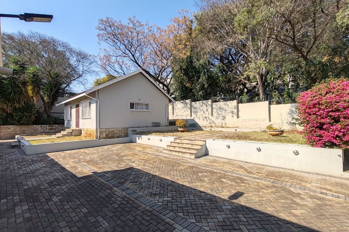 Rear exterior view featuring a paved driveway, tiered garden levels with retaining walls, and secure perimeter fencing.