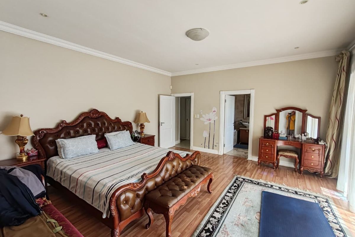 Spacious bedroom featuring laminate flooring, recessed downlighting, and decorative coving, with direct access to an en-suite bathroom.