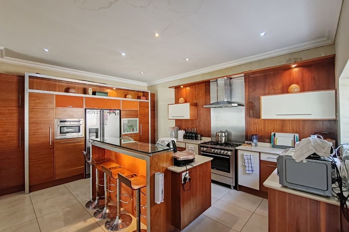 Spacious kitchen featuring wood-finish cabinetry, a central island with breakfast bar, stainless steel appliances, and stone countertops.