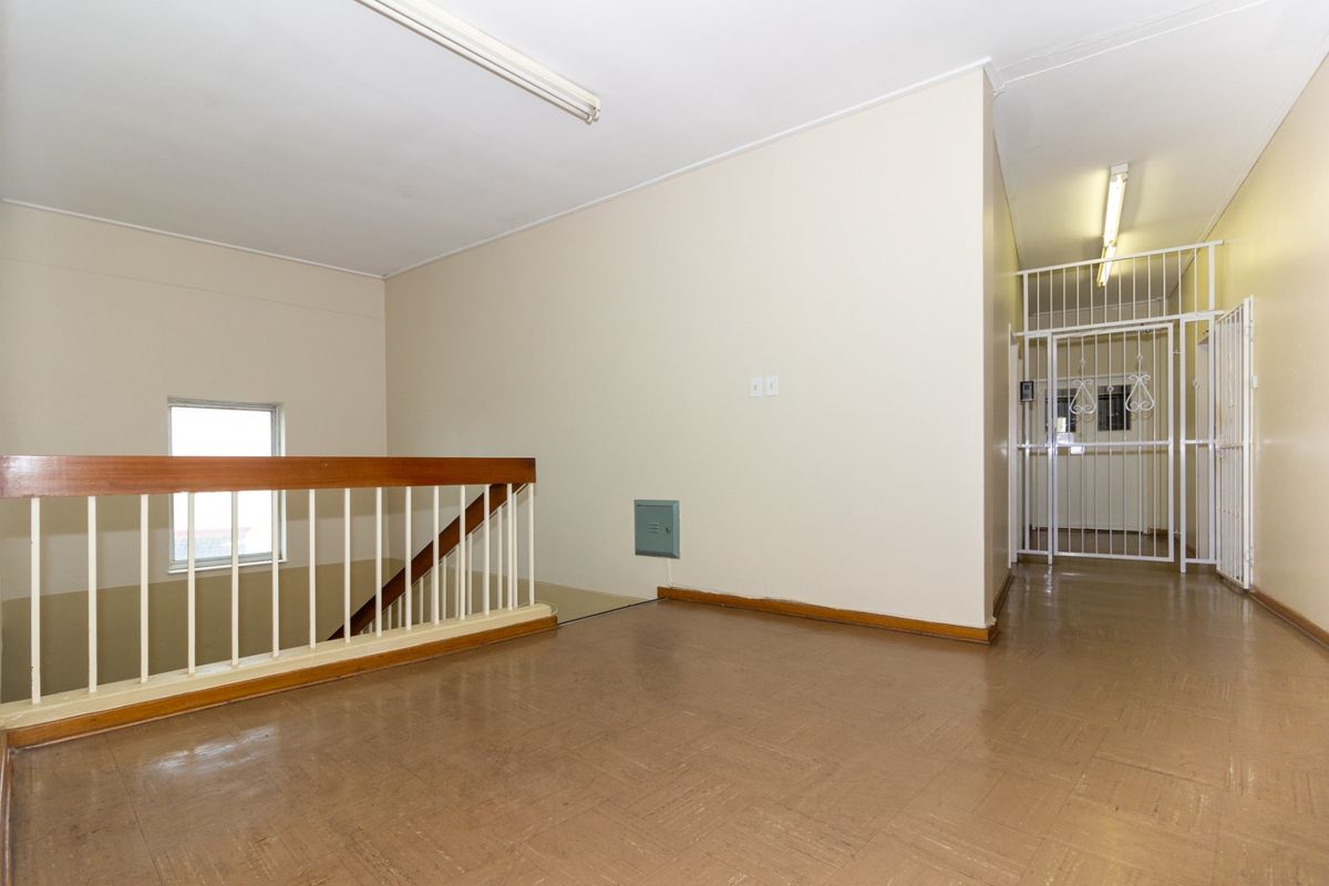 A vacant office hallway featuring vinyl flooring, a wooden balustrade overlooking the stairwell, and a secure metal gate entrance.