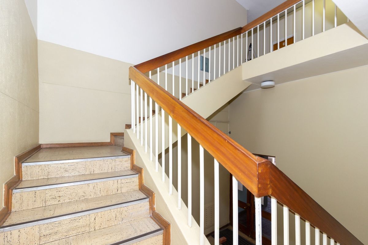 A functional office building stairwell featuring a wooden handrail, metal balustrade, and tiled stair treads, providing access between building levels.