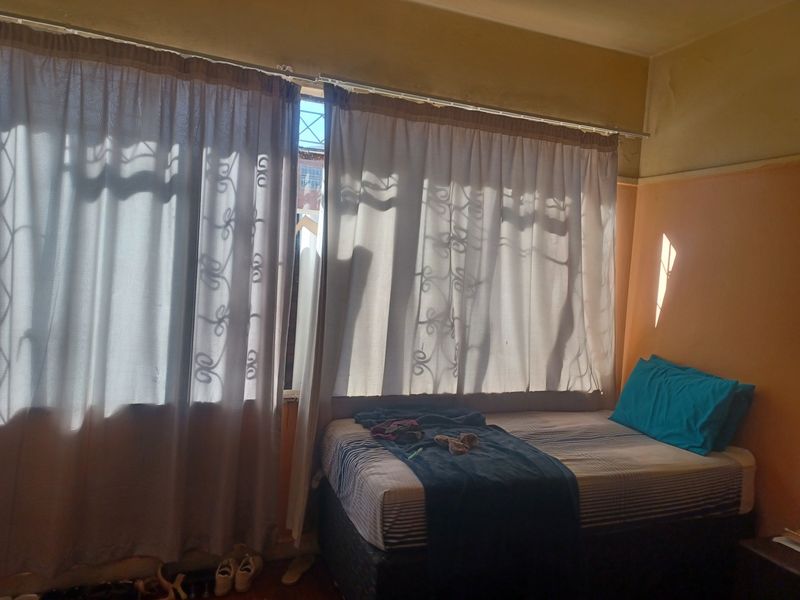 A bedroom featuring natural light through large windows with security bars and curtain rails, requiring cosmetic updates to the wall finishes.