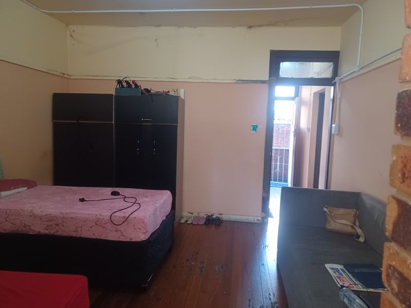 A bedroom featuring timber flooring and exposed electrical conduit, showing signs of wear and requiring cosmetic updates to the walls and ceiling.