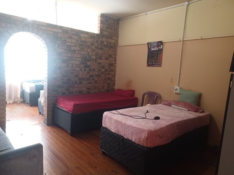 A bedroom featuring exposed brickwork, an arched entryway, and hardwood flooring, requiring cosmetic updates to improve the overall finish and aesthetic appeal.