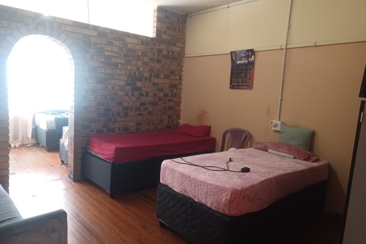 A bedroom featuring exposed brickwork, an arched entryway, and hardwood flooring, requiring cosmetic updates to improve the overall finish and aesthetic appeal.