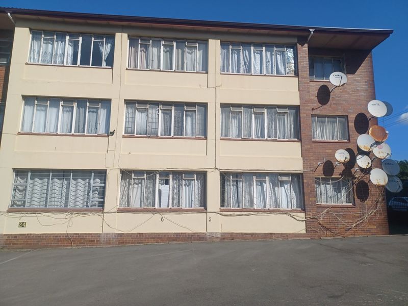 Exterior view of a multi-story apartment building featuring brick and painted facade, metal-framed windows with security bars, and multiple satellite dish installations.