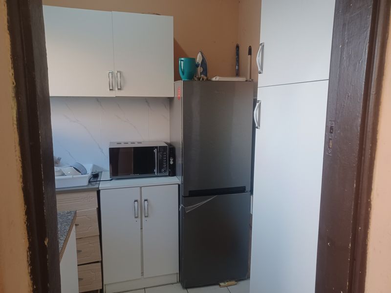 A compact kitchen featuring white built-in cabinetry, laminate countertops, and a tiled backsplash, providing functional storage and preparation space.