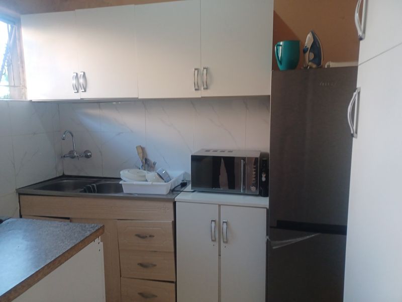 A compact kitchen featuring white cabinetry, laminate countertops, a stainless steel sink, and tiled backsplash, requiring minor cosmetic updates.