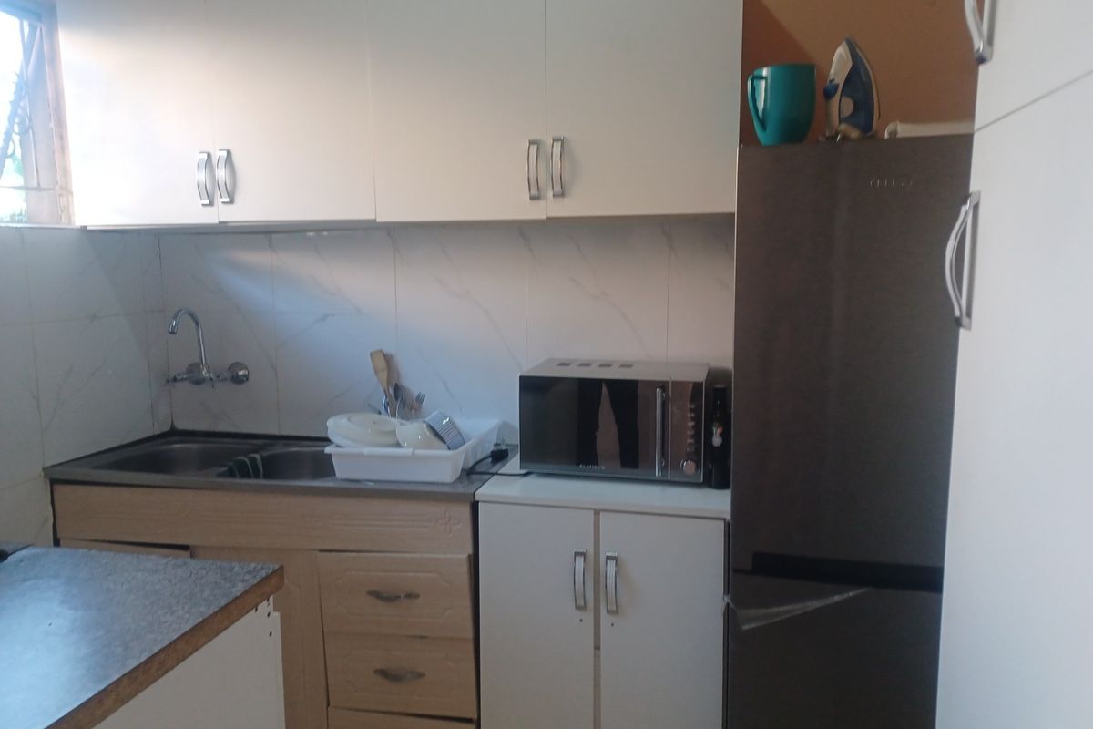 A compact kitchen featuring white cabinetry, laminate countertops, a stainless steel sink, and tiled backsplash, requiring minor cosmetic updates.