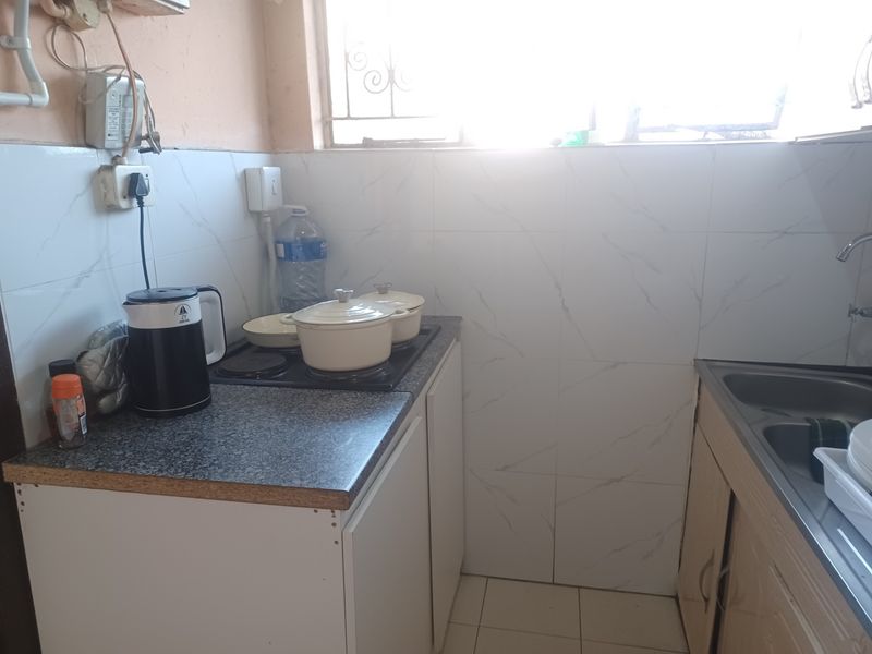 A compact kitchen featuring a built-in hob, stainless steel sink, and tiled splashback, requiring cosmetic updates to improve its overall condition and appeal.