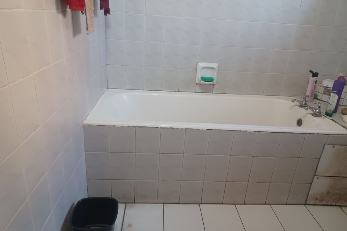 A dated bathroom featuring a standard bathtub with tiled surround and flooring, requiring cosmetic updates and repairs to the wall and tile finishes.