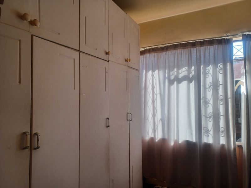 A bedroom featuring floor-to-ceiling built-in cupboards and a window fitted with security bars.