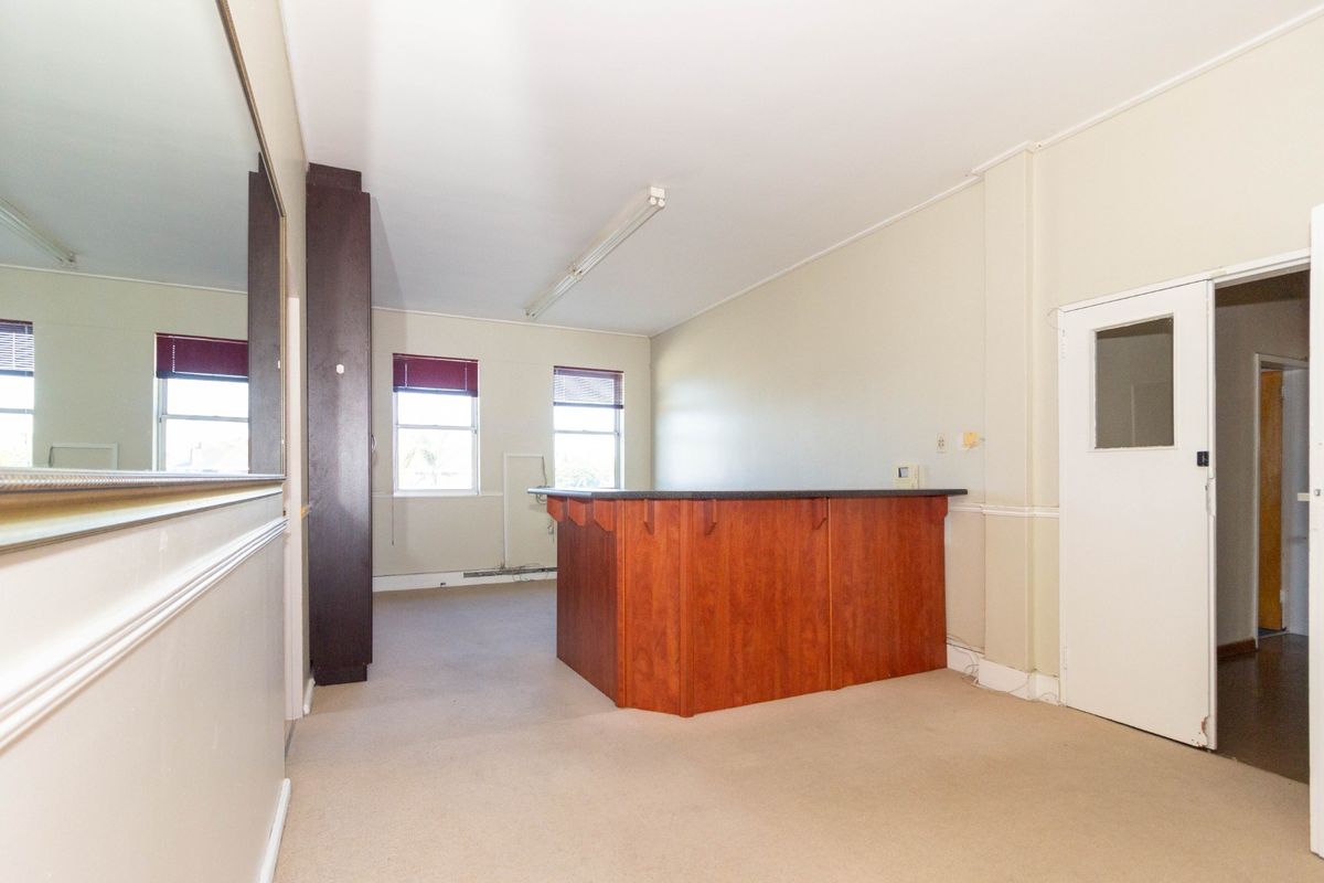 An open-plan office space featuring a built-in reception counter, neutral wall finishes, and fluorescent lighting, suitable for a professional workspace.