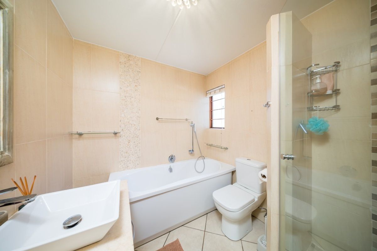 A well-maintained bathroom featuring a bathtub, separate glass-enclosed shower, vessel sink, and neutral wall and floor tiling.