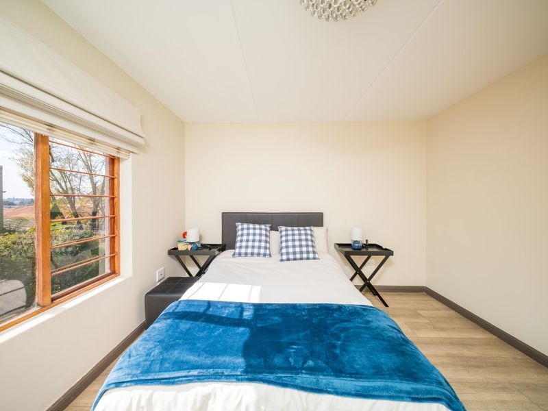 A well-lit bedroom featuring laminate flooring, neutral walls, and a large window with timber frames, providing a comfortable and functional living space.
