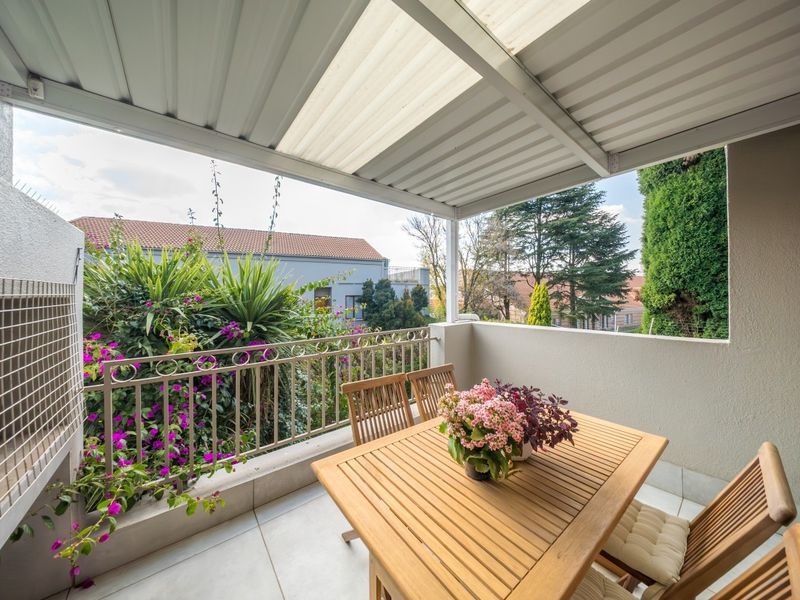 A covered balcony featuring tiled flooring, a metal balustrade, and a corrugated roof with a translucent panel, offering a pleasant outdoor seating area.
